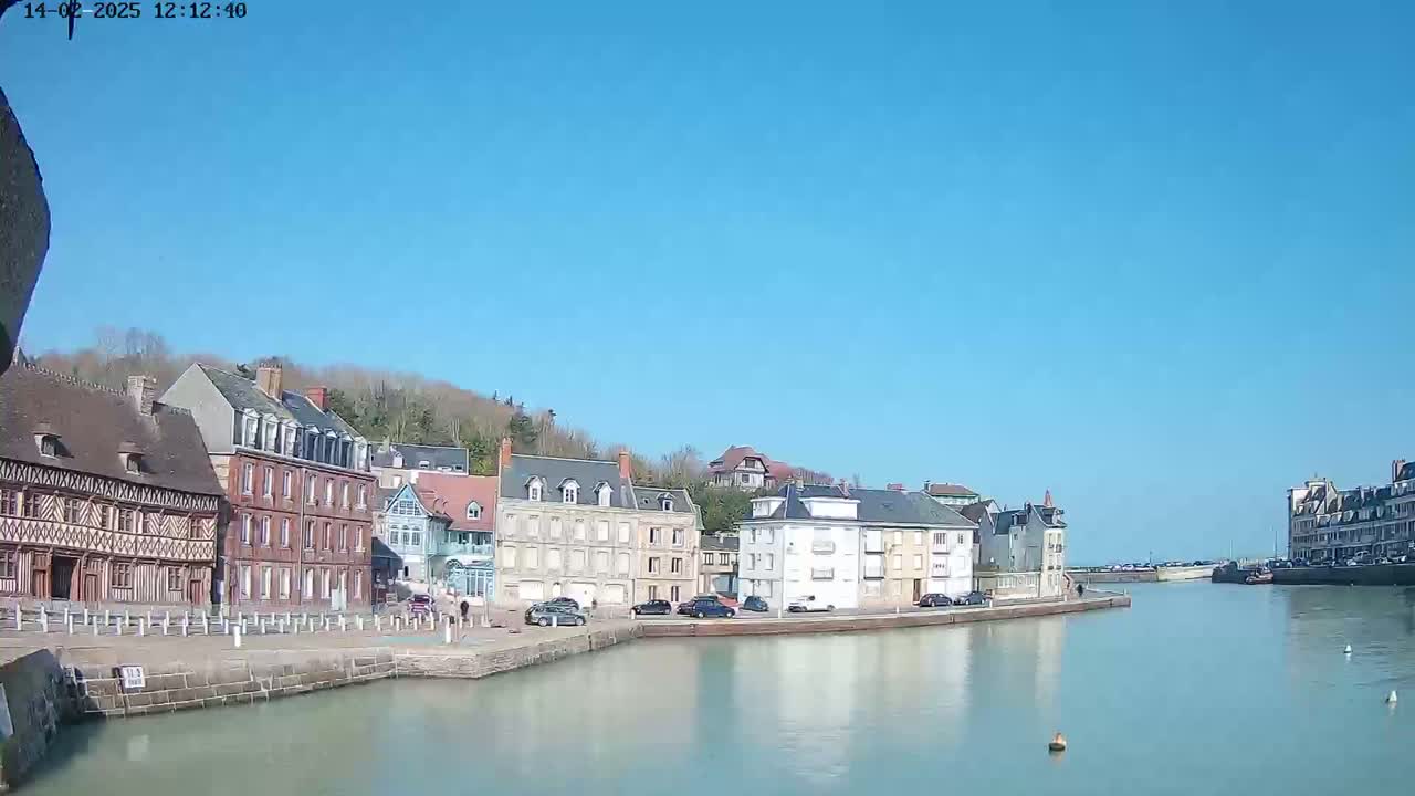 A waterfront town with several buildings lines a calm waterway under a clear blue sky.