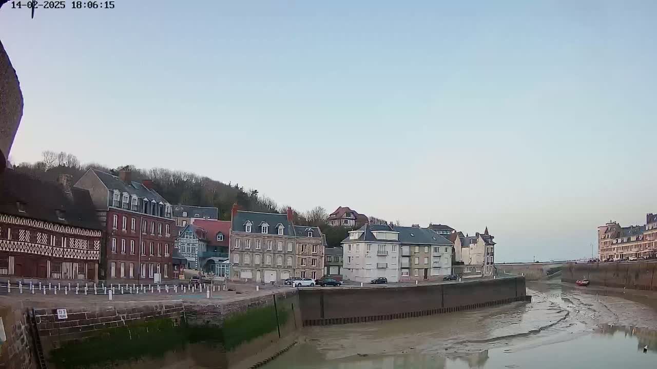 A calm, clear day reveals a waterfront town with several multi-story buildings lining a narrow waterway at low tide.