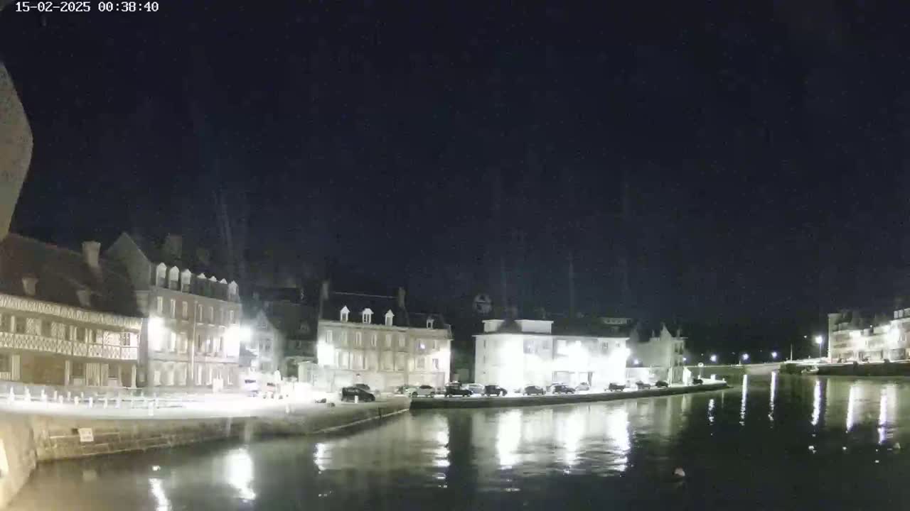 A nighttime view of a calm canal reflecting brightly lit buildings along its banks under a dark sky.