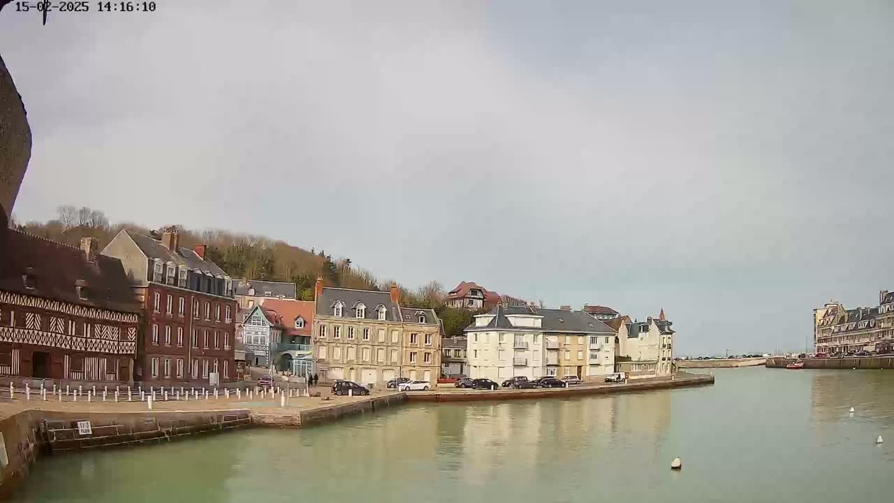 A calm waterway flows past a row of multi-story buildings under a pale, overcast sky.
