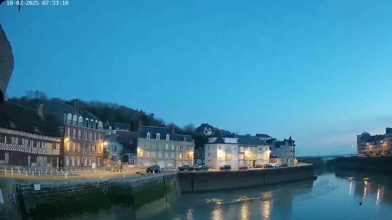 Under a twilight sky, a calm river flows past a waterfront lined with buildings, some with lights on.