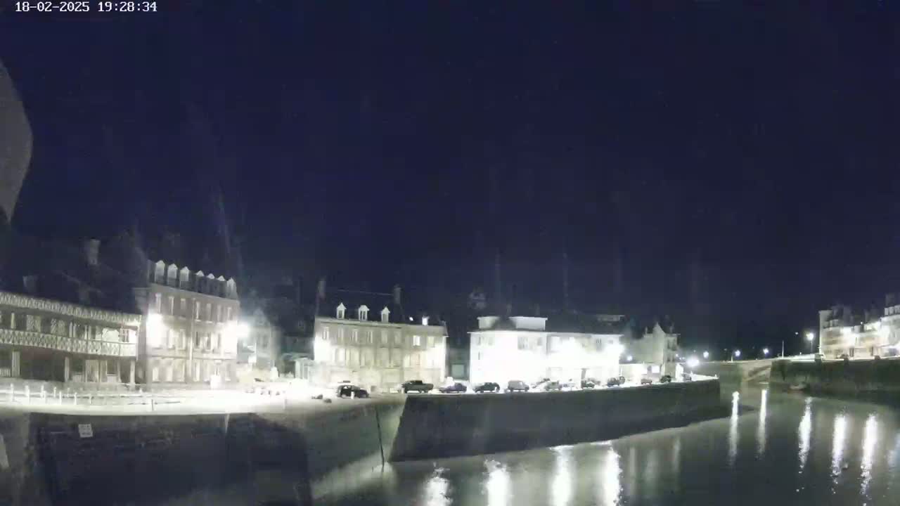 A nighttime view of a waterfront town with several buildings illuminated along a calm body of water.