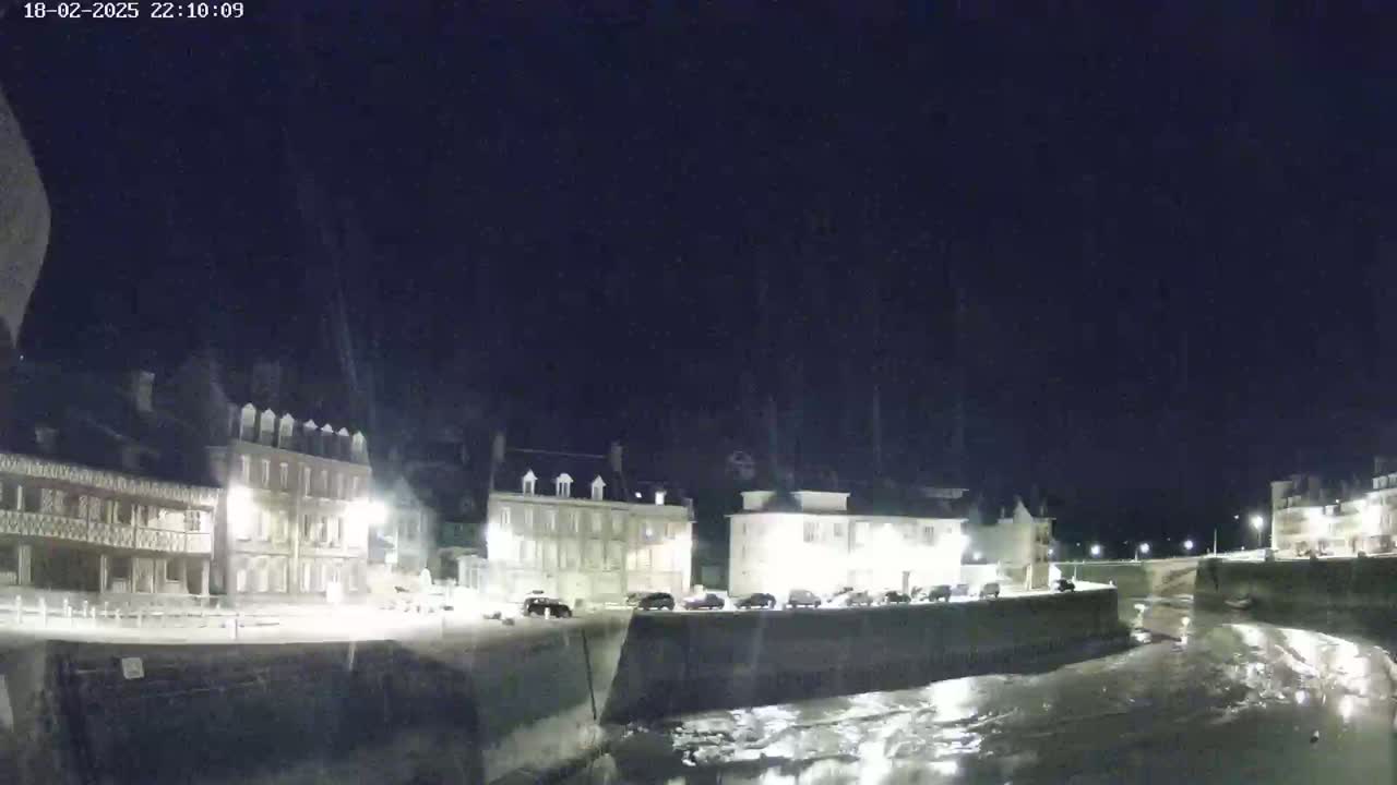 A nighttime view of a waterway bordered by buildings under a dark, possibly snowy sky.