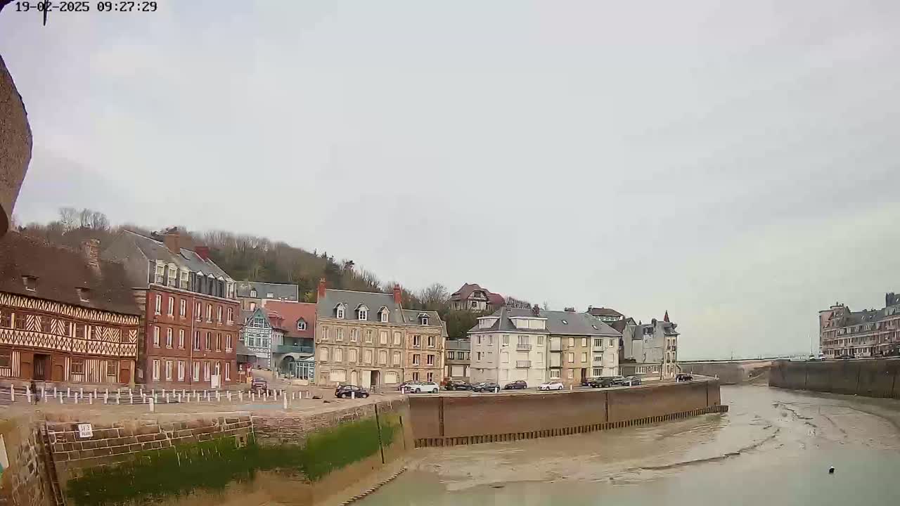 A row of multi-story buildings lines a waterway with low tide under an overcast sky.