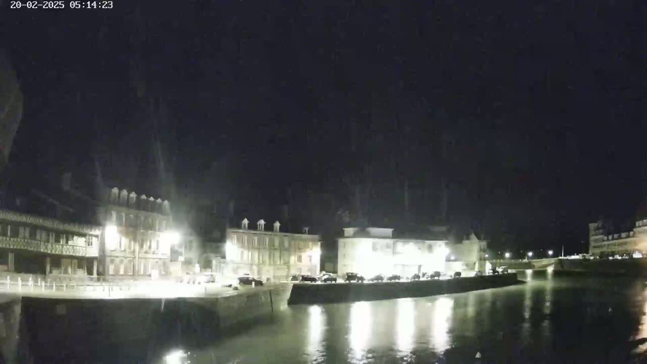 At night, a calm body of water reflects the lights of buildings lining its edge.