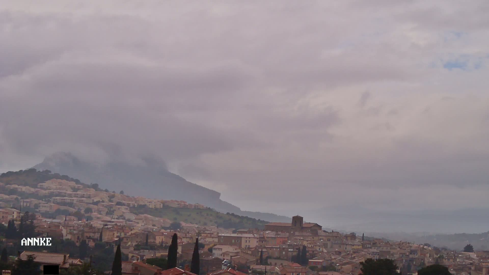 A hillside town with a church is visible beneath a heavily overcast sky.