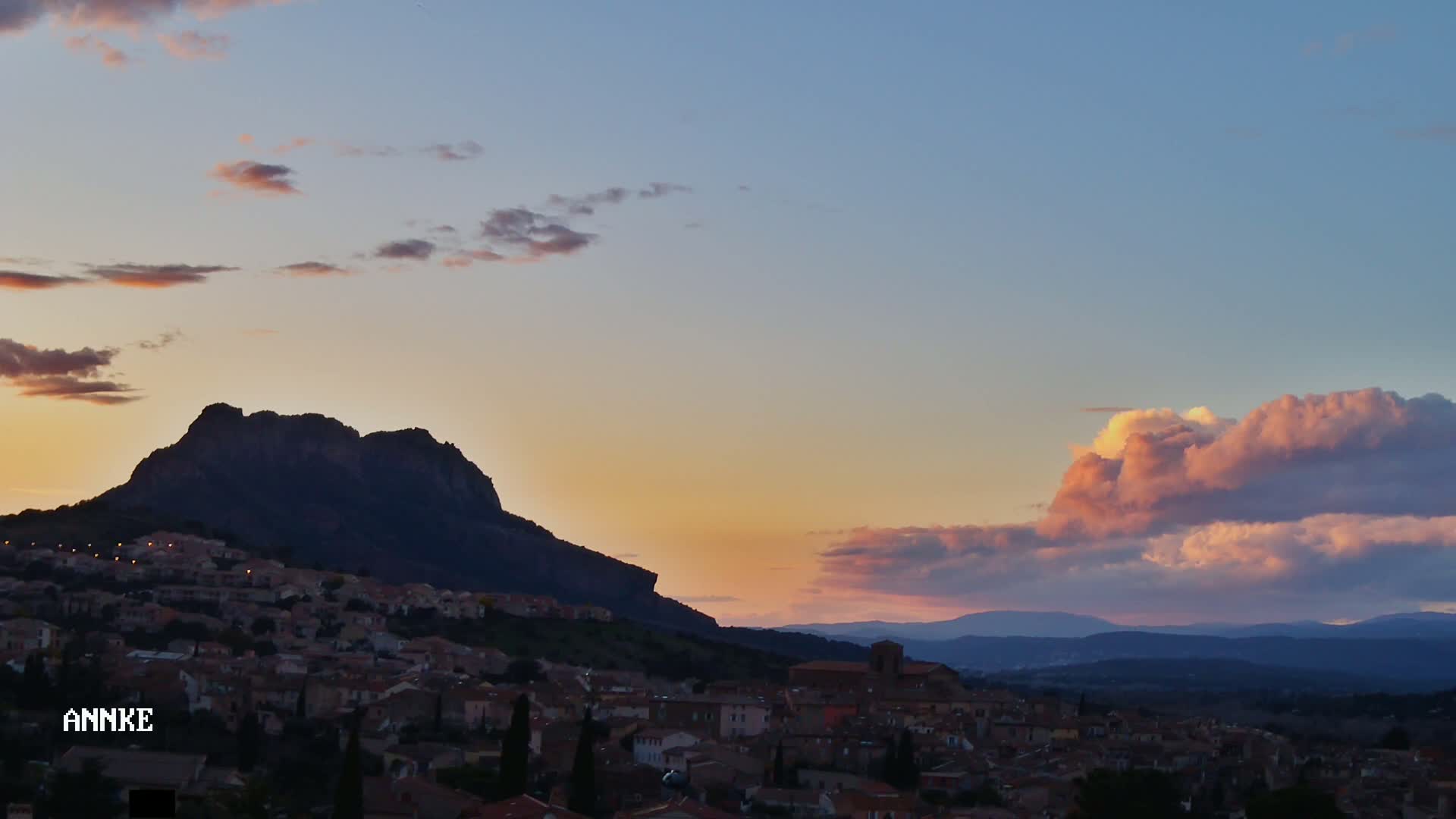 A hilltop town is silhouetted against a sunset sky with pink and orange clouds.