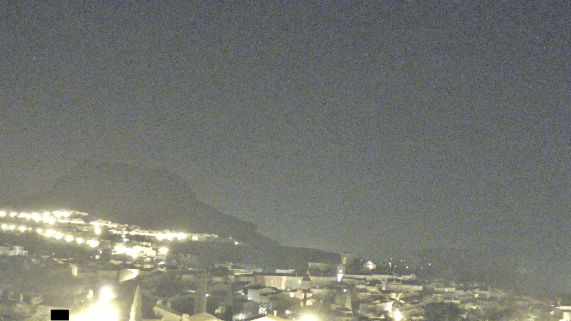 A nighttime view of a town nestled against a hill under a clear, dark sky.