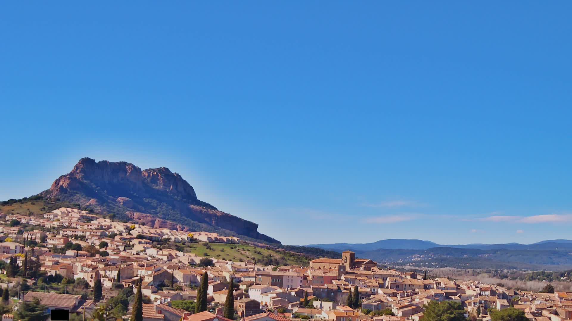 A small town nestled at the base of a large, rocky mountain under a clear blue sky.