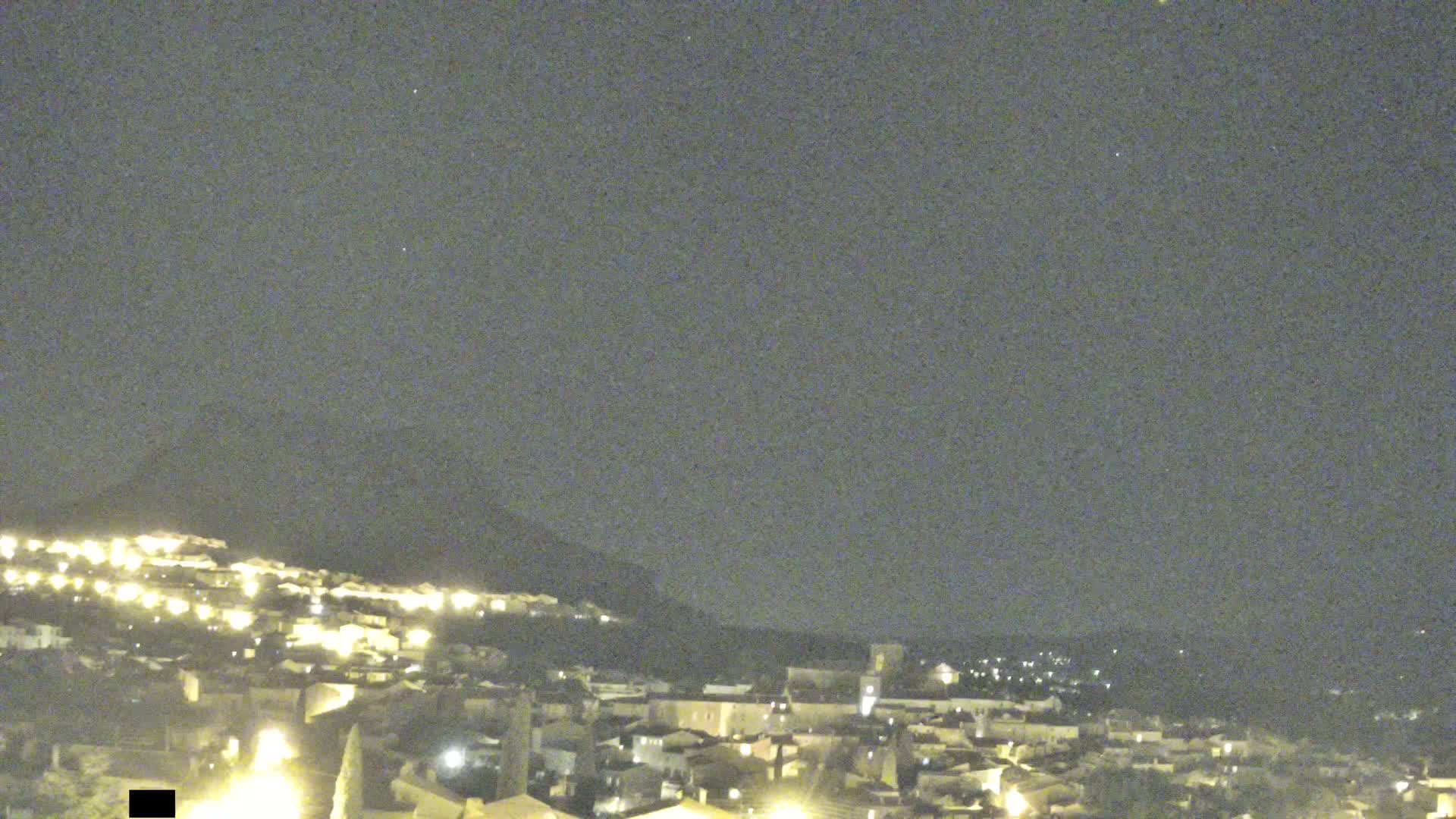 A nighttime view of a town nestled on a hill under a clear, dark sky.