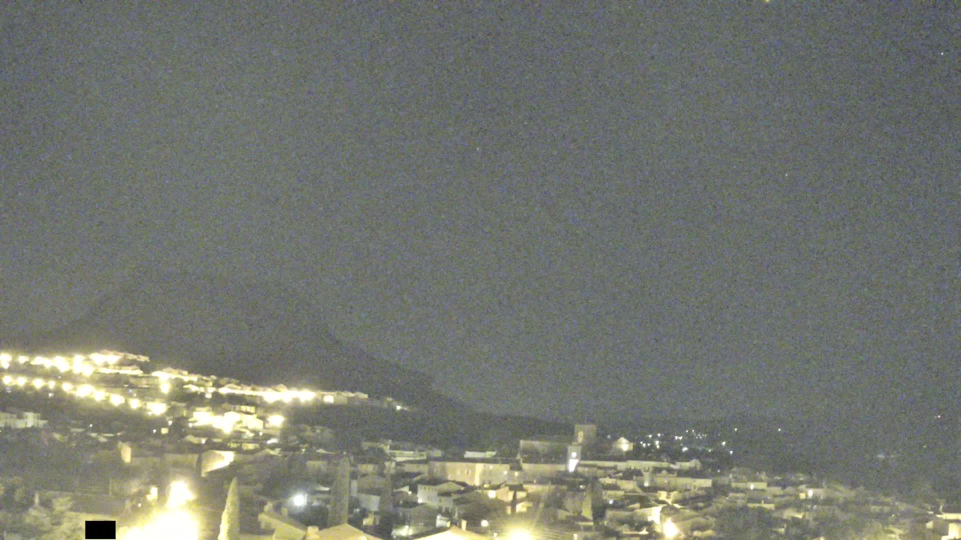 A nighttime view of a town nestled on a hillside under a dark, clear sky.