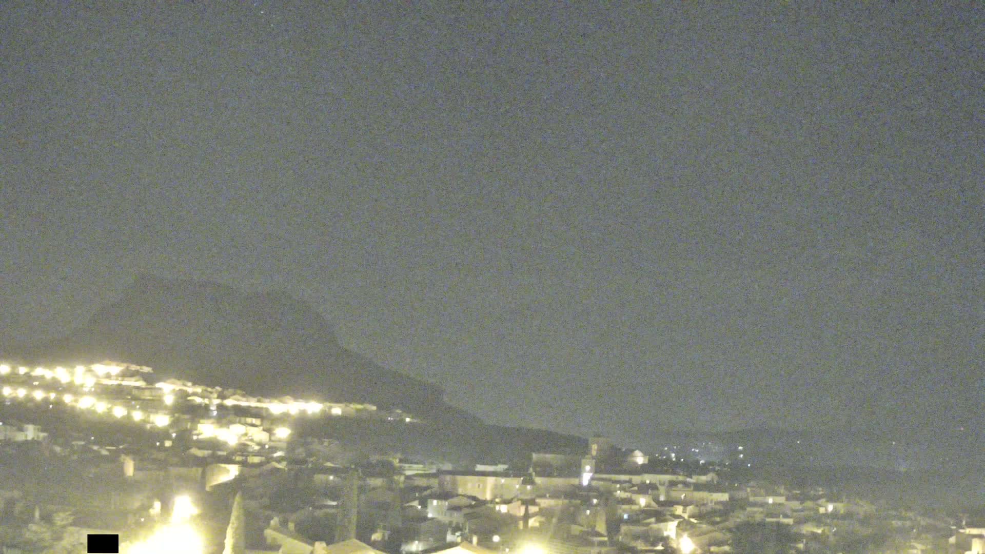 A nighttime view of a town nestled at the base of a hill under a mostly clear sky.