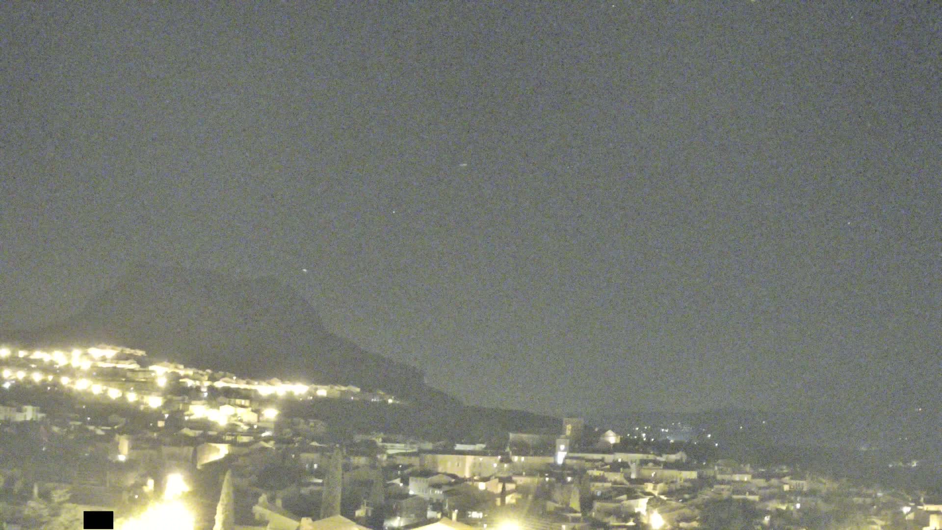 A nighttime view of a town nestled against a hill under a clear, dark sky.
