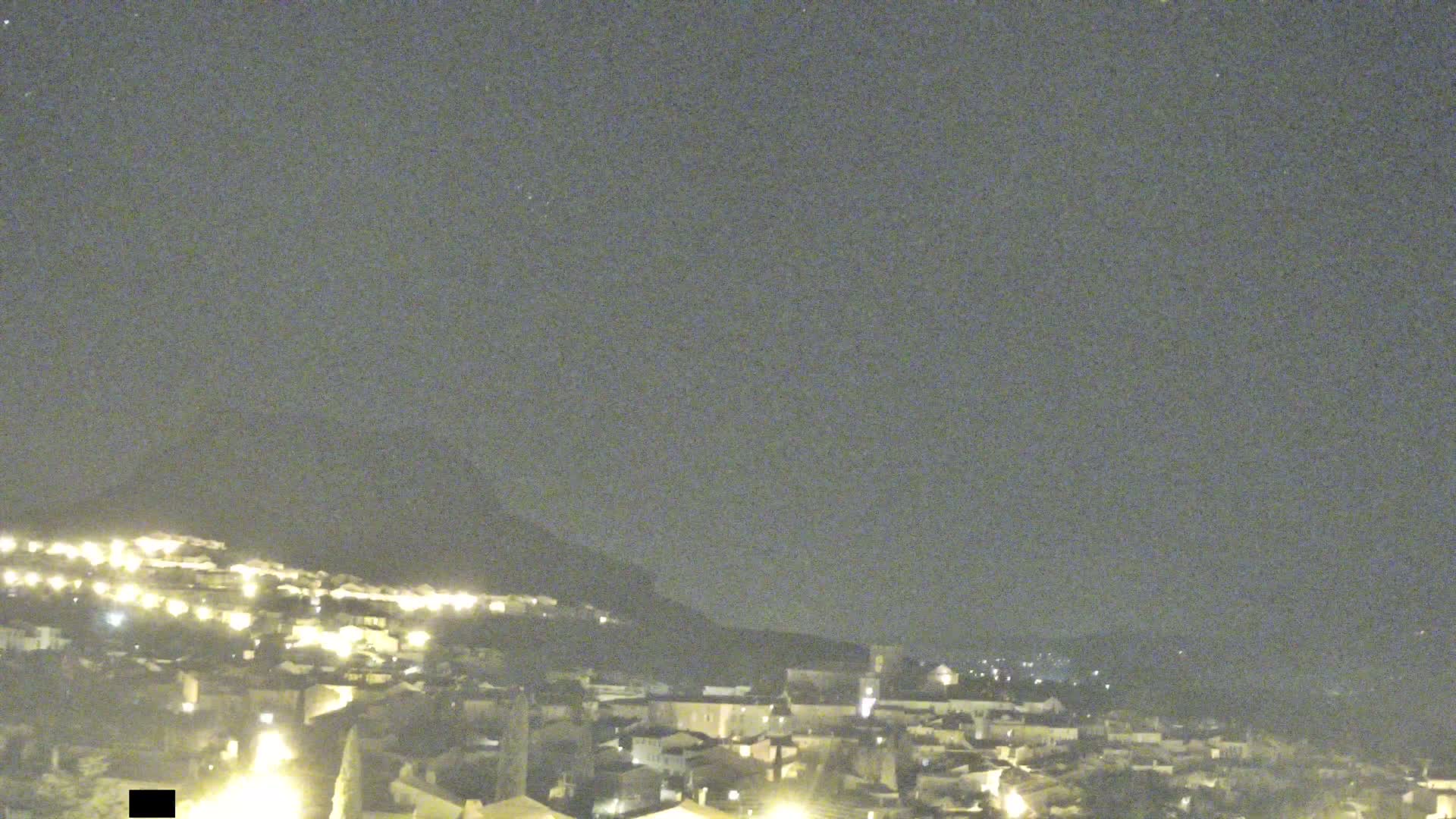 A nighttime view of a town nestled against a hill under a clear, dark sky.