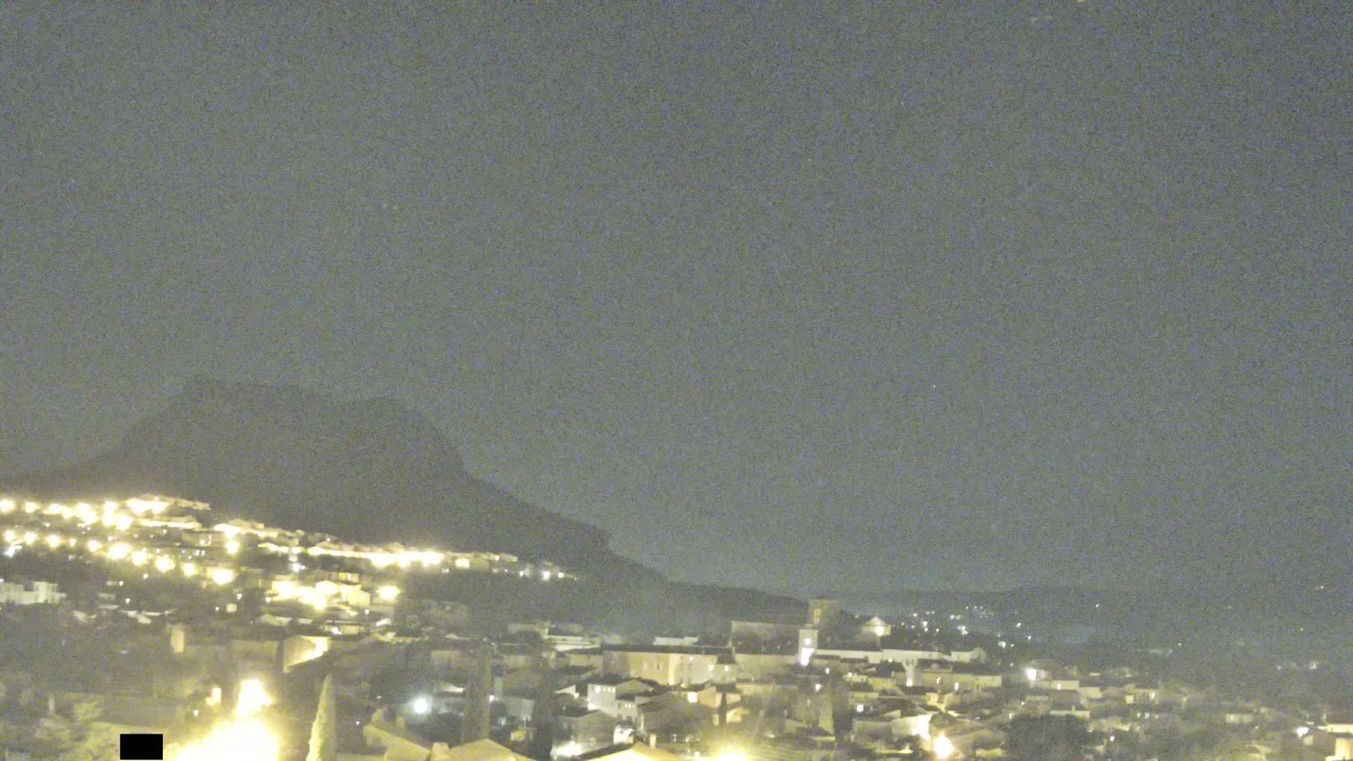 A nighttime view of a small town nestled against a hill under a clear, dark sky.