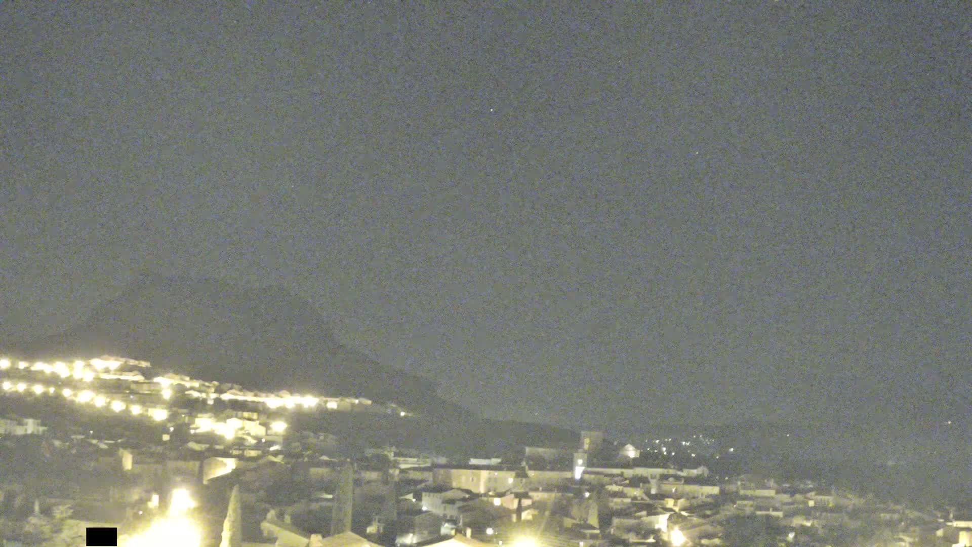A nighttime view of a town nestled on a hillside under a clear, dark sky.