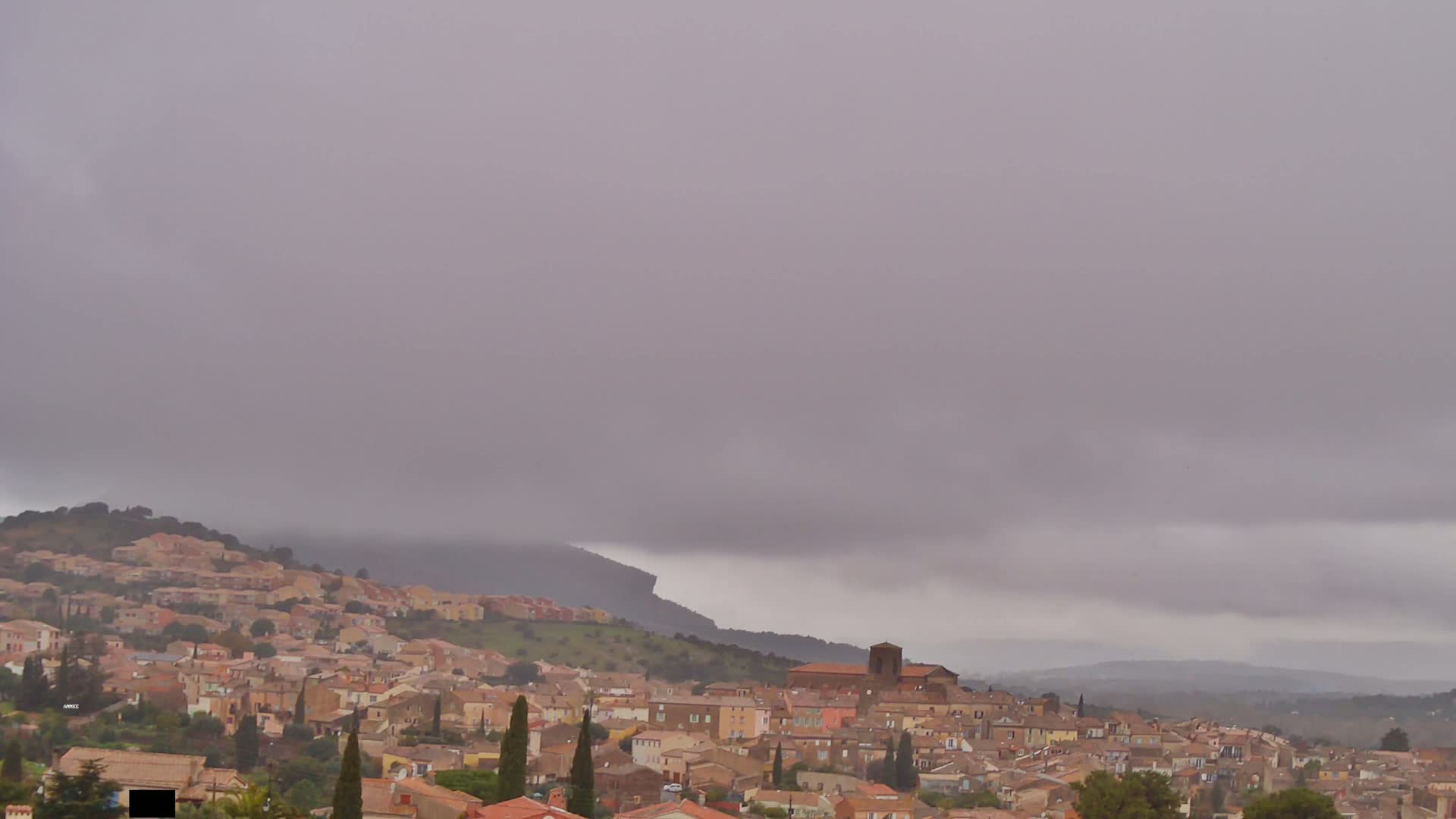 A sprawling town of tan buildings nestled into rolling hills under a low, overcast sky.