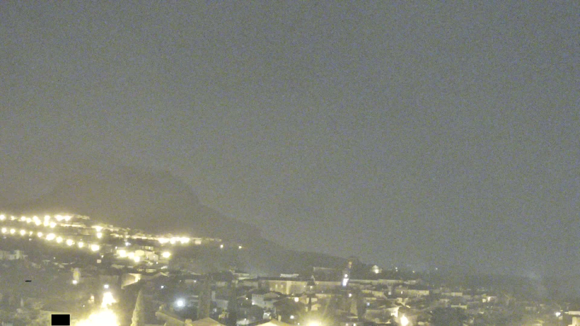 A nighttime view of a hazy town nestled against a hill, illuminated by scattered lights.