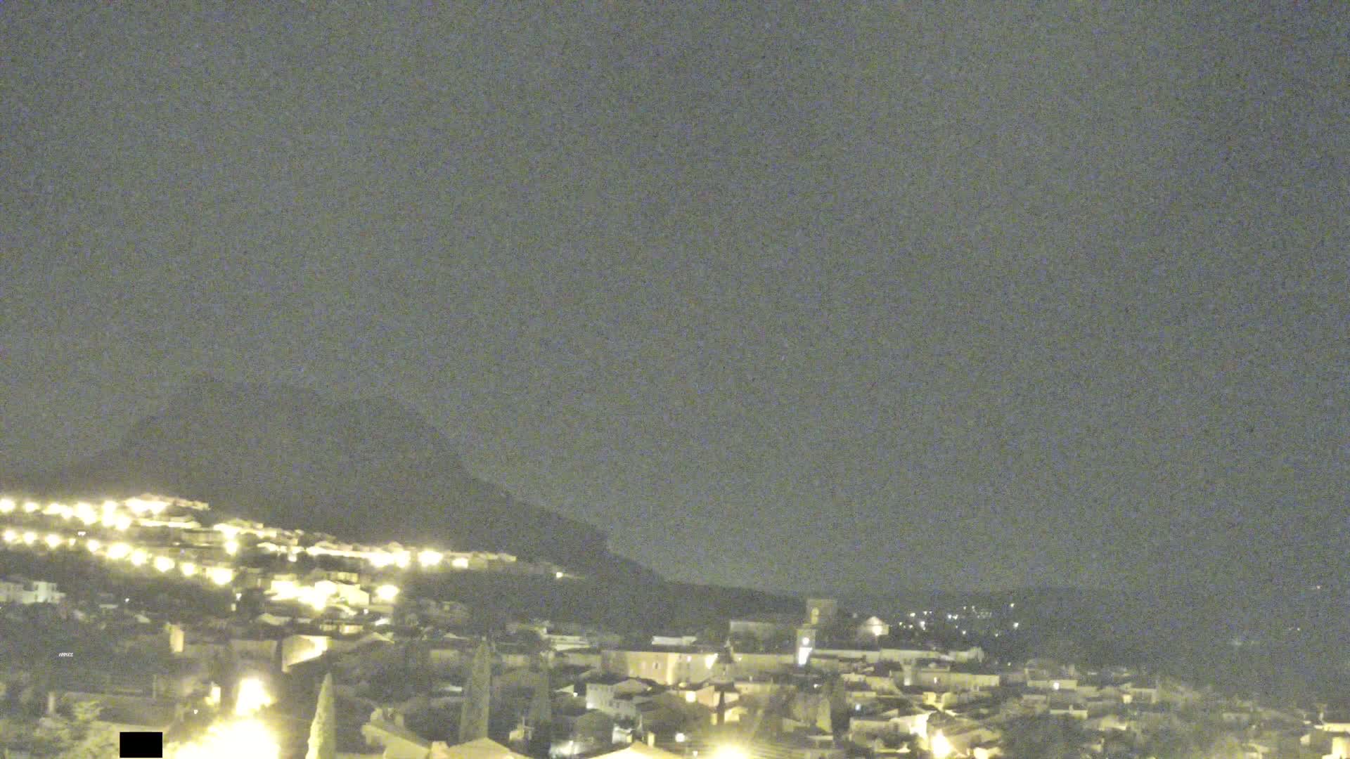 A nighttime view of a town nestled against a hill under a dark, overcast sky.
