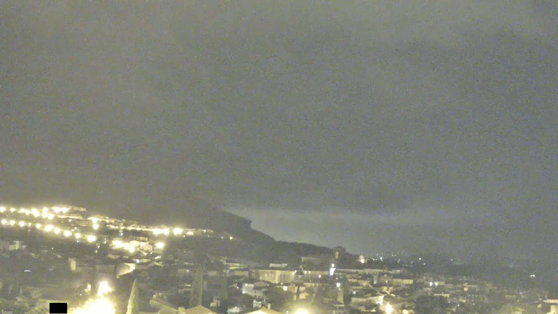 A nighttime view of a town nestled against a hill under an overcast sky.