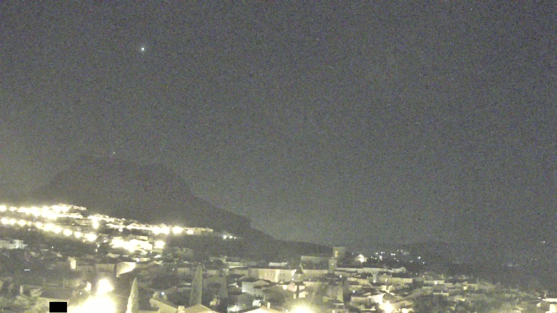 A nighttime view of a hilltop town illuminated by lights under a clear, dark sky.