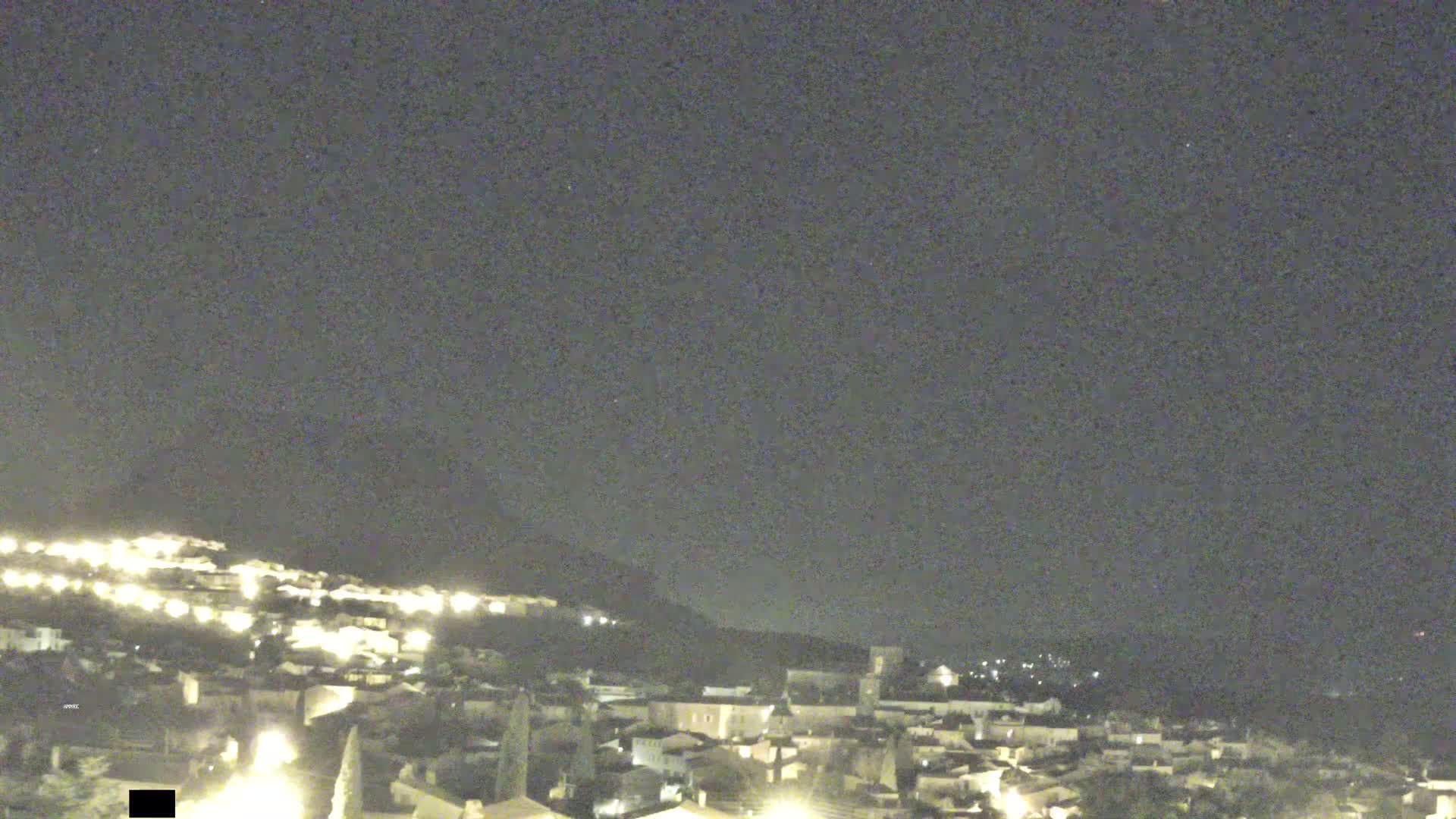 A nighttime view of a town illuminated by lights, situated on a hill under a clear, dark sky.
