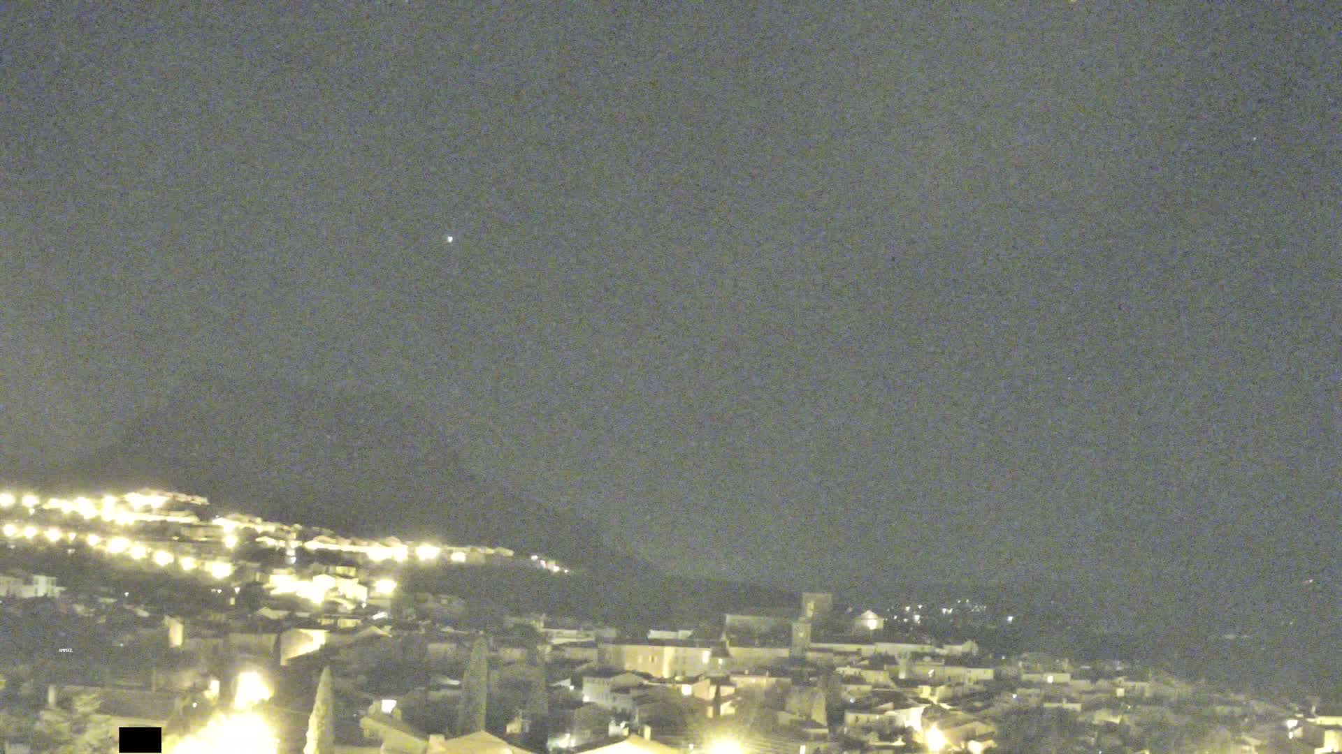 A hillside town is illuminated at night under a clear, dark sky.