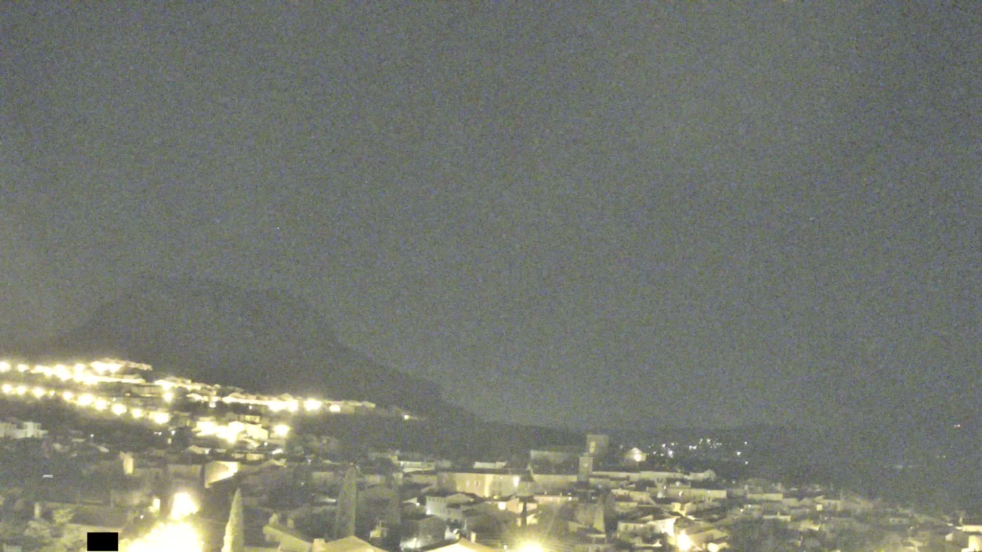 A nighttime view of a hilltop town with its lights illuminated under a dark, clear sky.