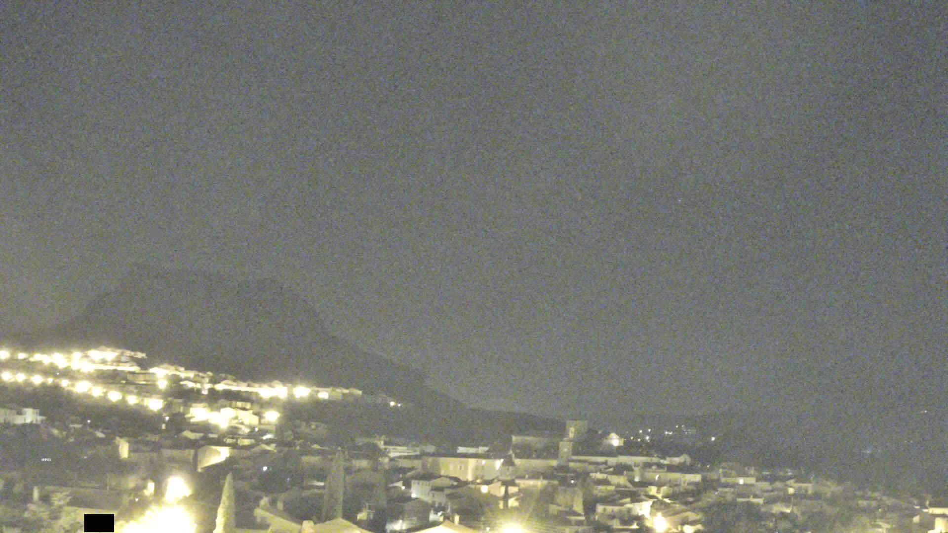 A nighttime view of a town nestled against a hill, under a mostly clear sky.