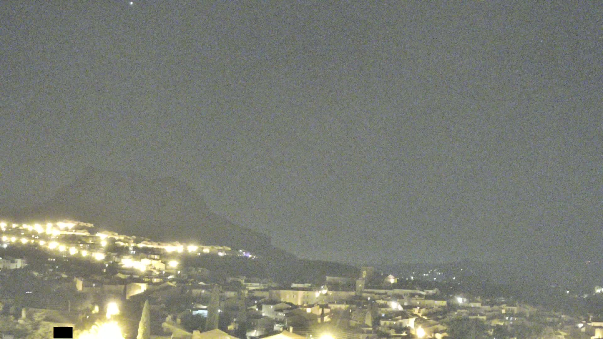 A nighttime view of a hilltop town illuminated by many small lights under a mostly clear, dark sky.
