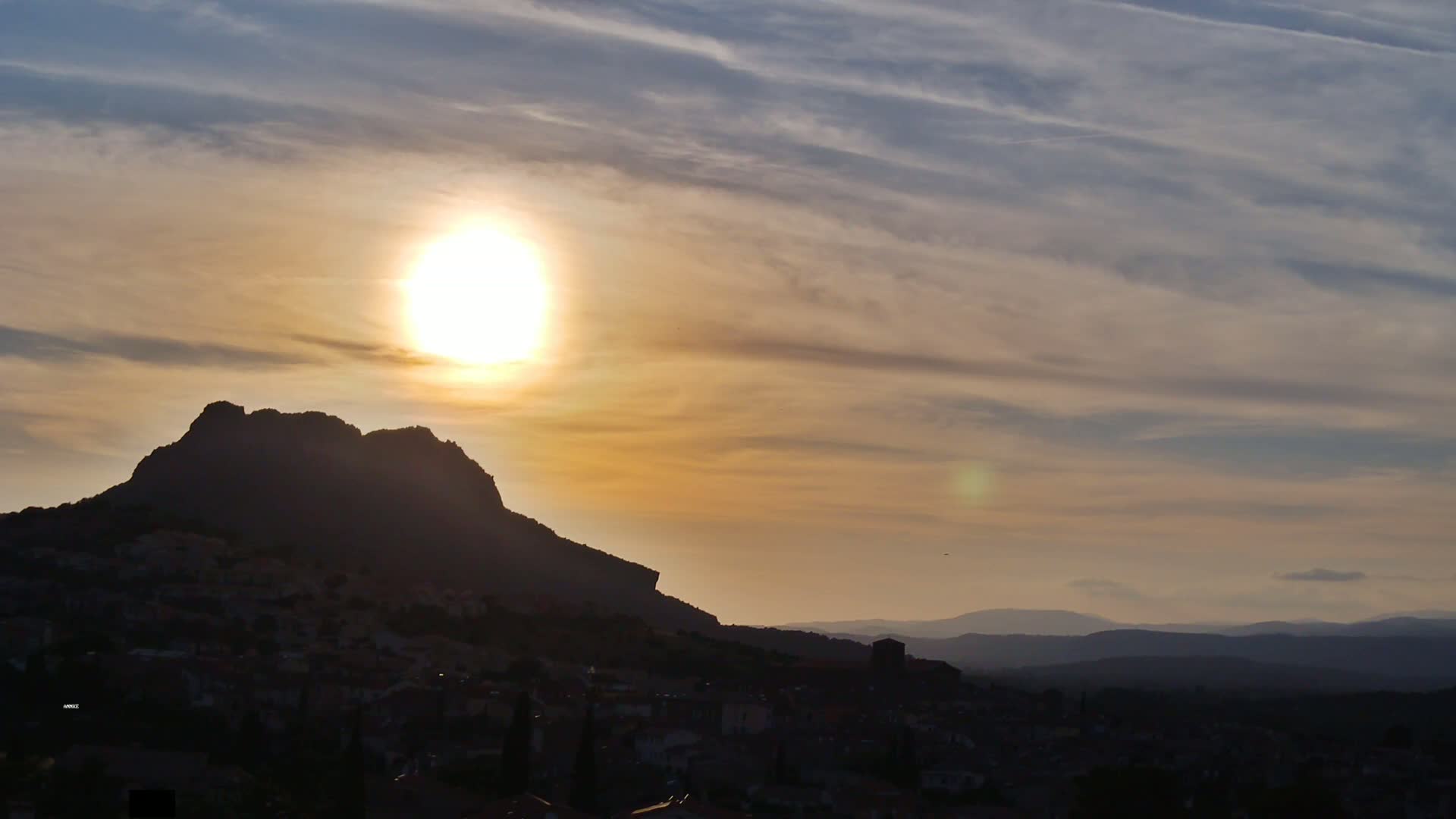 A large, dark mountain silhouetted against a sunset sky with thin, wispy clouds.