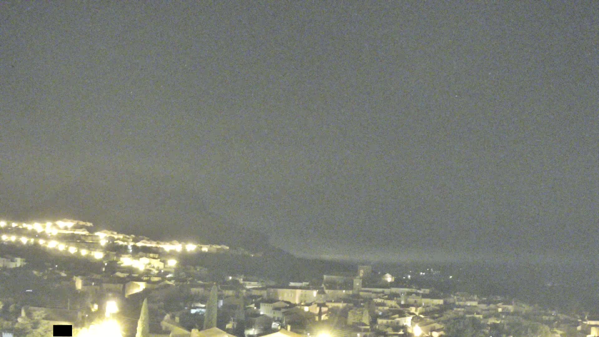 A nighttime, long shot of a hillside town with a hazy sky.