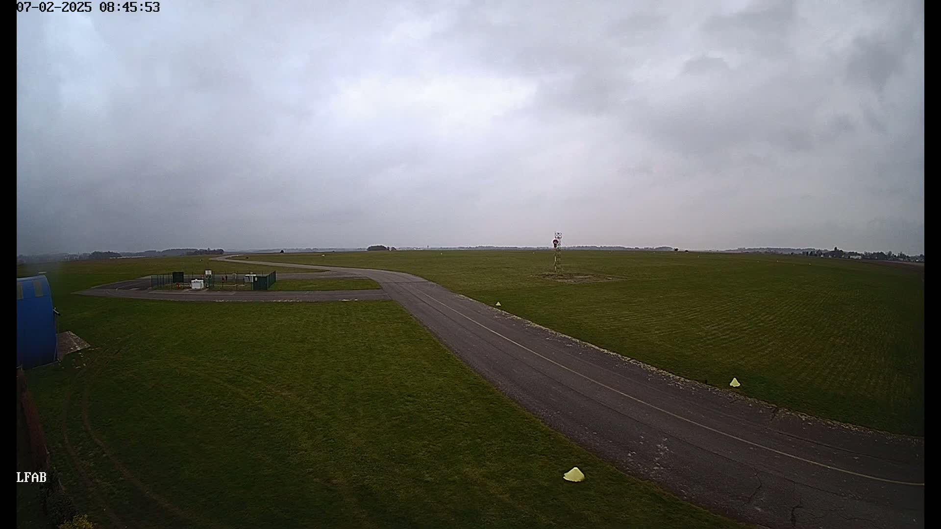 A paved road curves through a grassy airfield under an overcast sky.