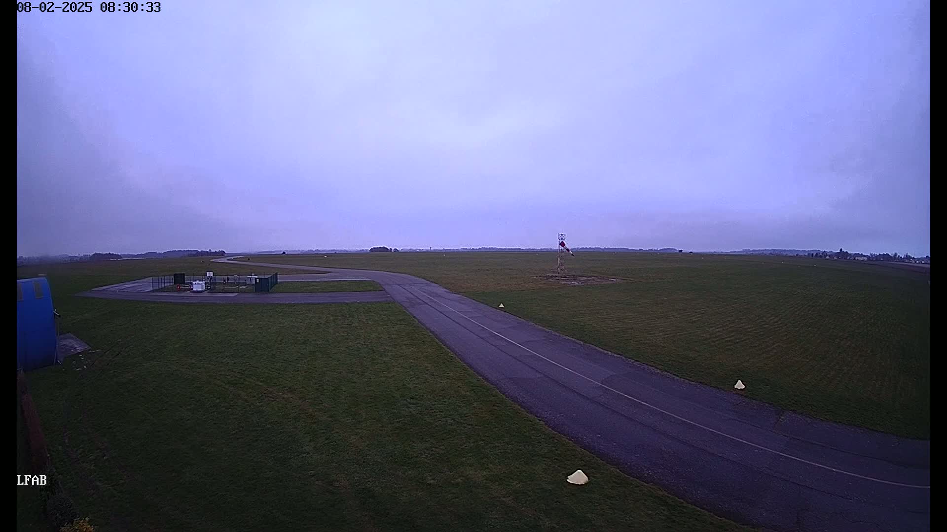 An airfield taxiway under a dusky sky curves through a grassy field.