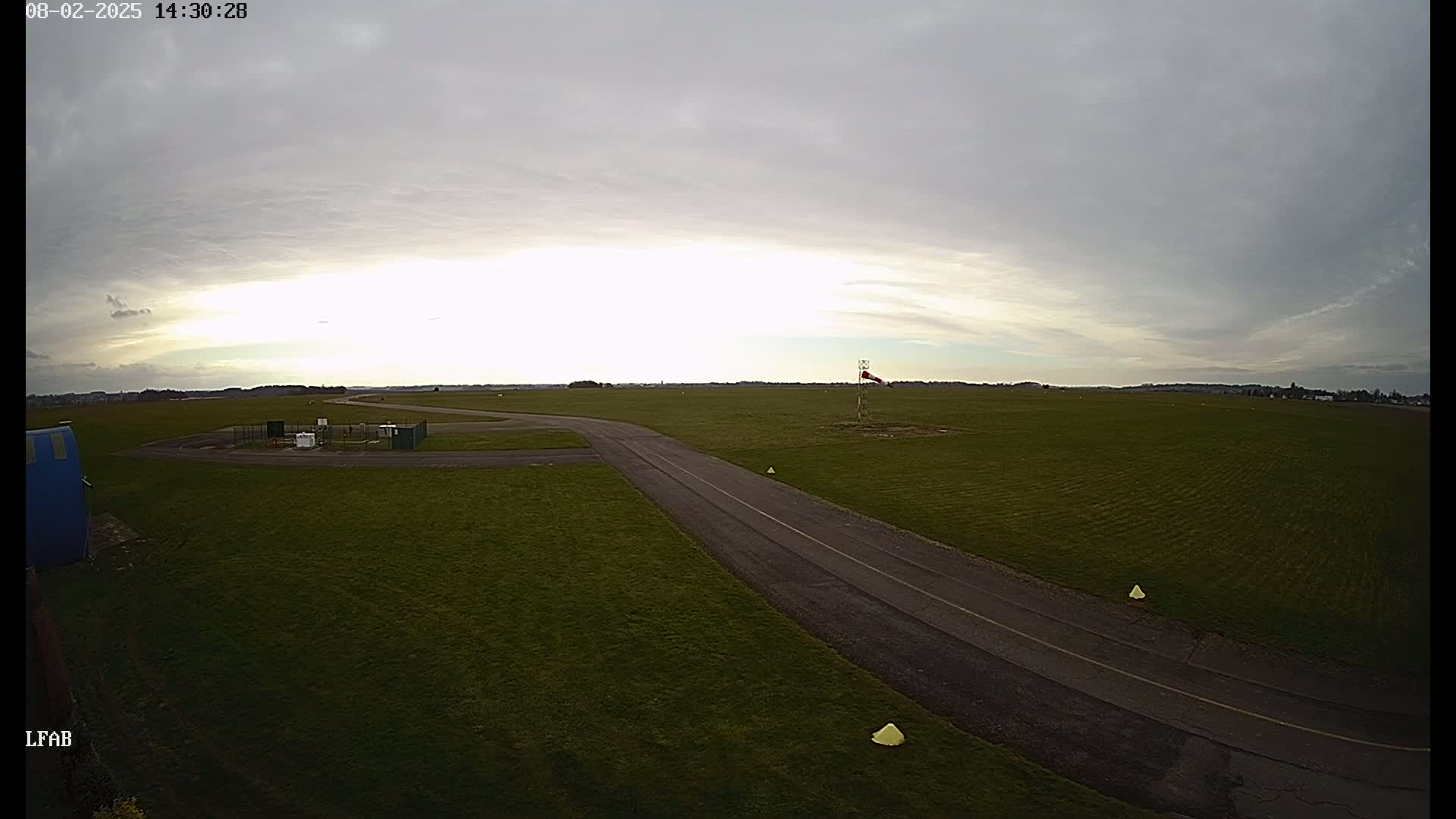 A paved road curves through a grassy airfield under a mostly cloudy sky.