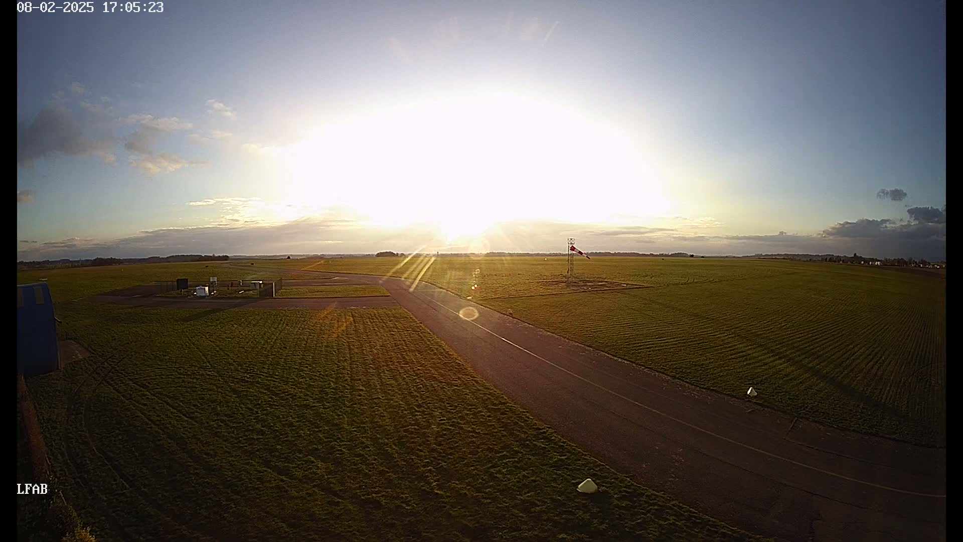A paved road cuts through a grassy airfield at sunset under a partly cloudy sky.