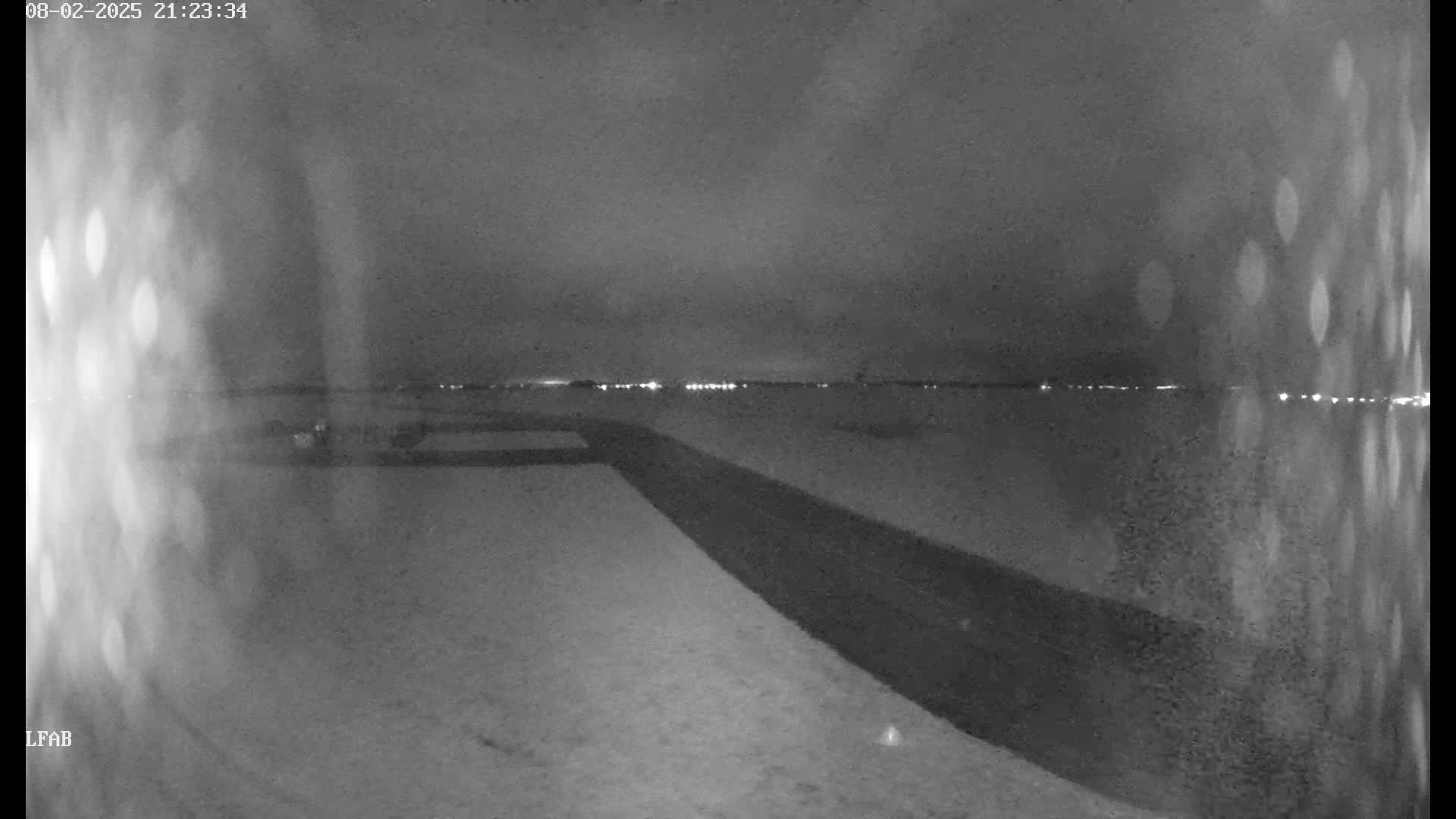 A nighttime, snow-covered landscape is visible, showing a dark road leading towards a distant line of lights under a cloudy sky.