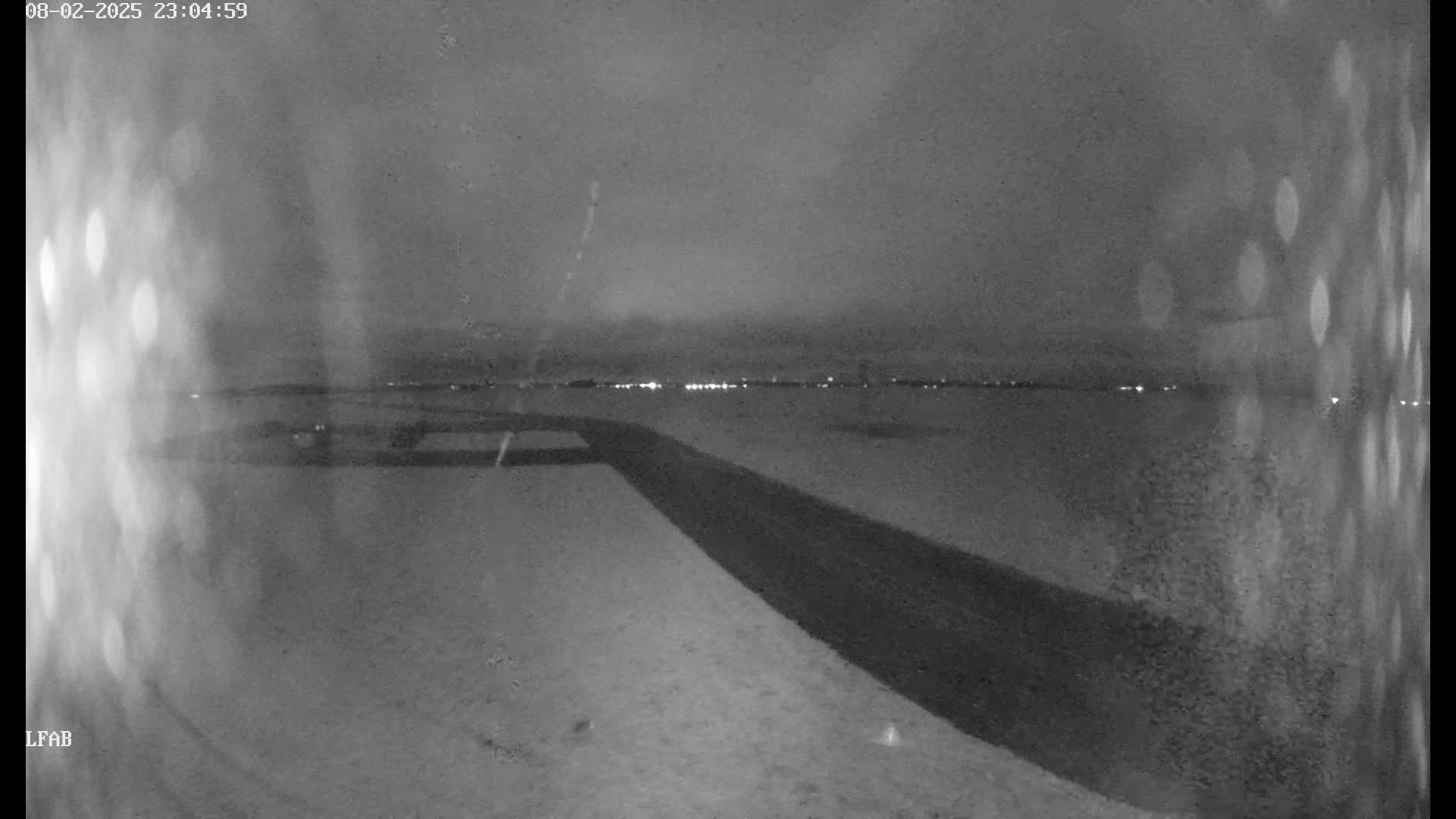 A dark, snowy landscape at night is illuminated by distant lights on the horizon.