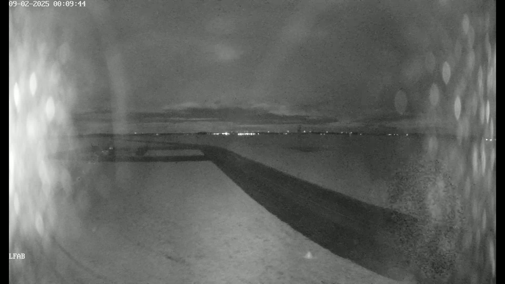 A dark, snowy landscape at night is shown with a road and distant lights.
