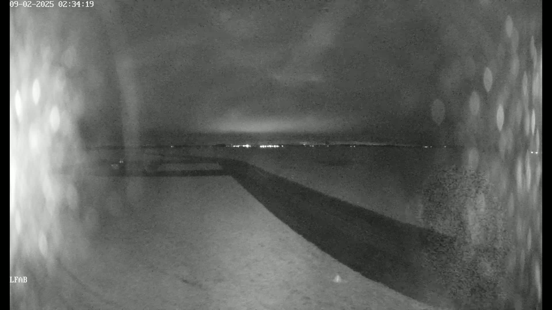 A nighttime, snow-covered landscape is visible, featuring a dark road or path extending toward a distant line of lights under a cloudy sky.