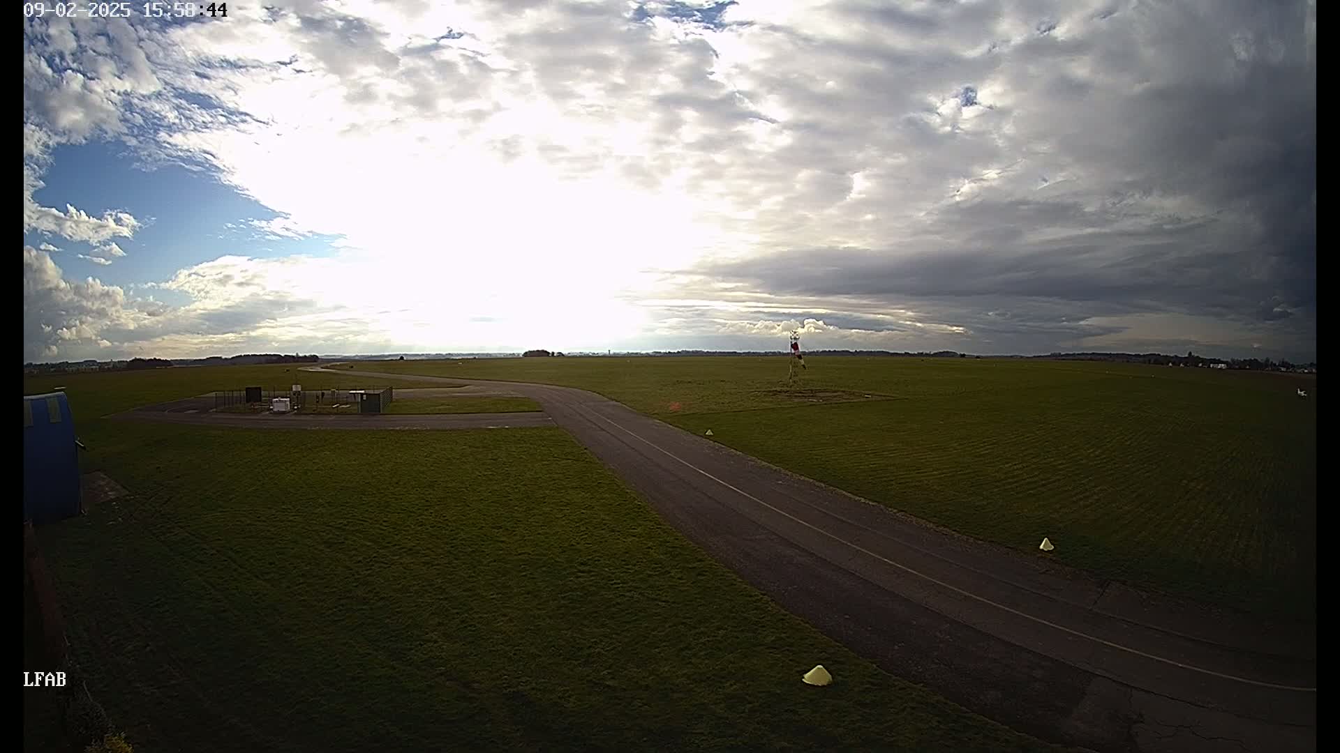 A paved road curves through a grassy airfield under a partly cloudy sky.