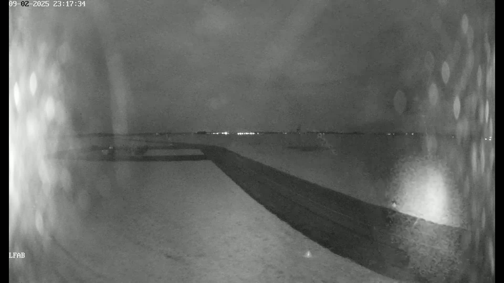 A snow-covered ground slopes down to a dark road at night, with distant lights visible on the horizon under a cloudy sky.