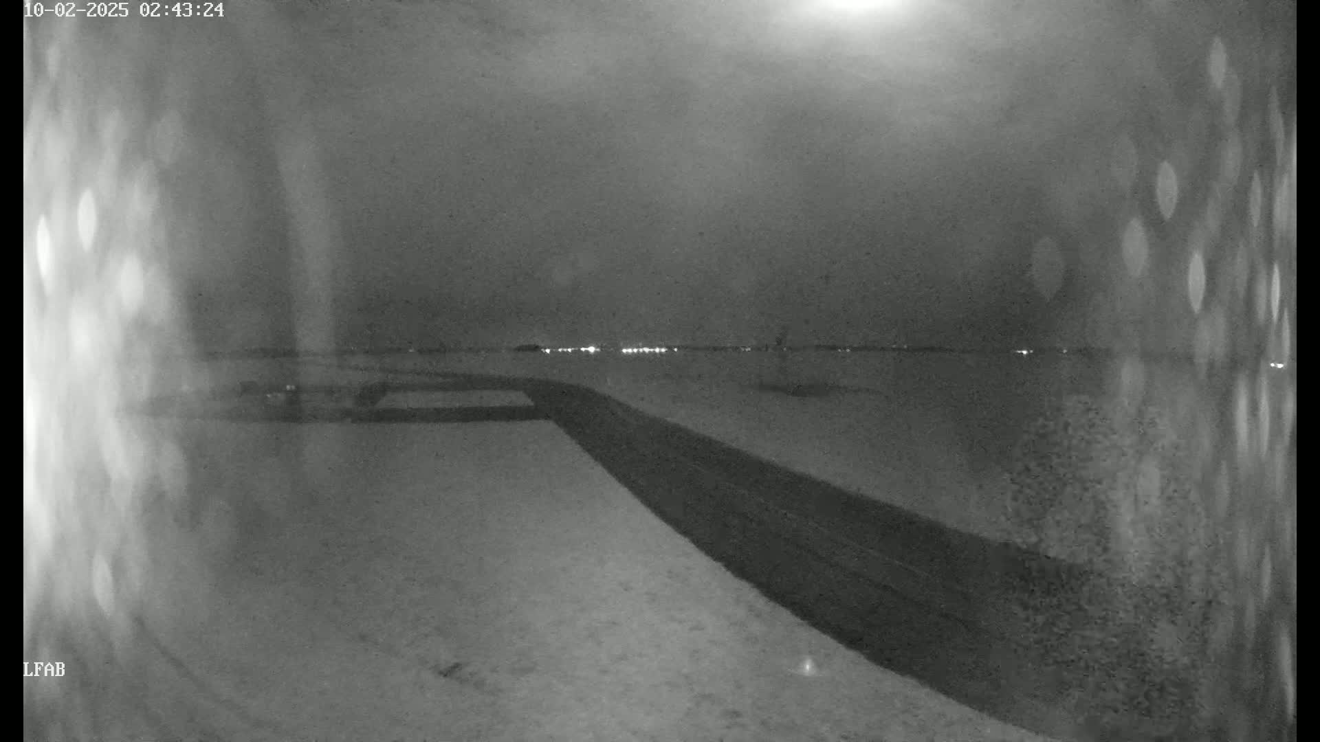 A dark, snowy landscape at night is shown with a road curving into the distance towards faintly visible lights.