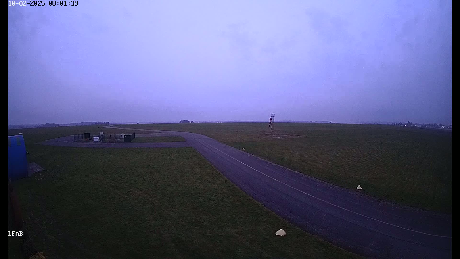A paved taxiway curves across a grassy airfield under a hazy, twilight sky.