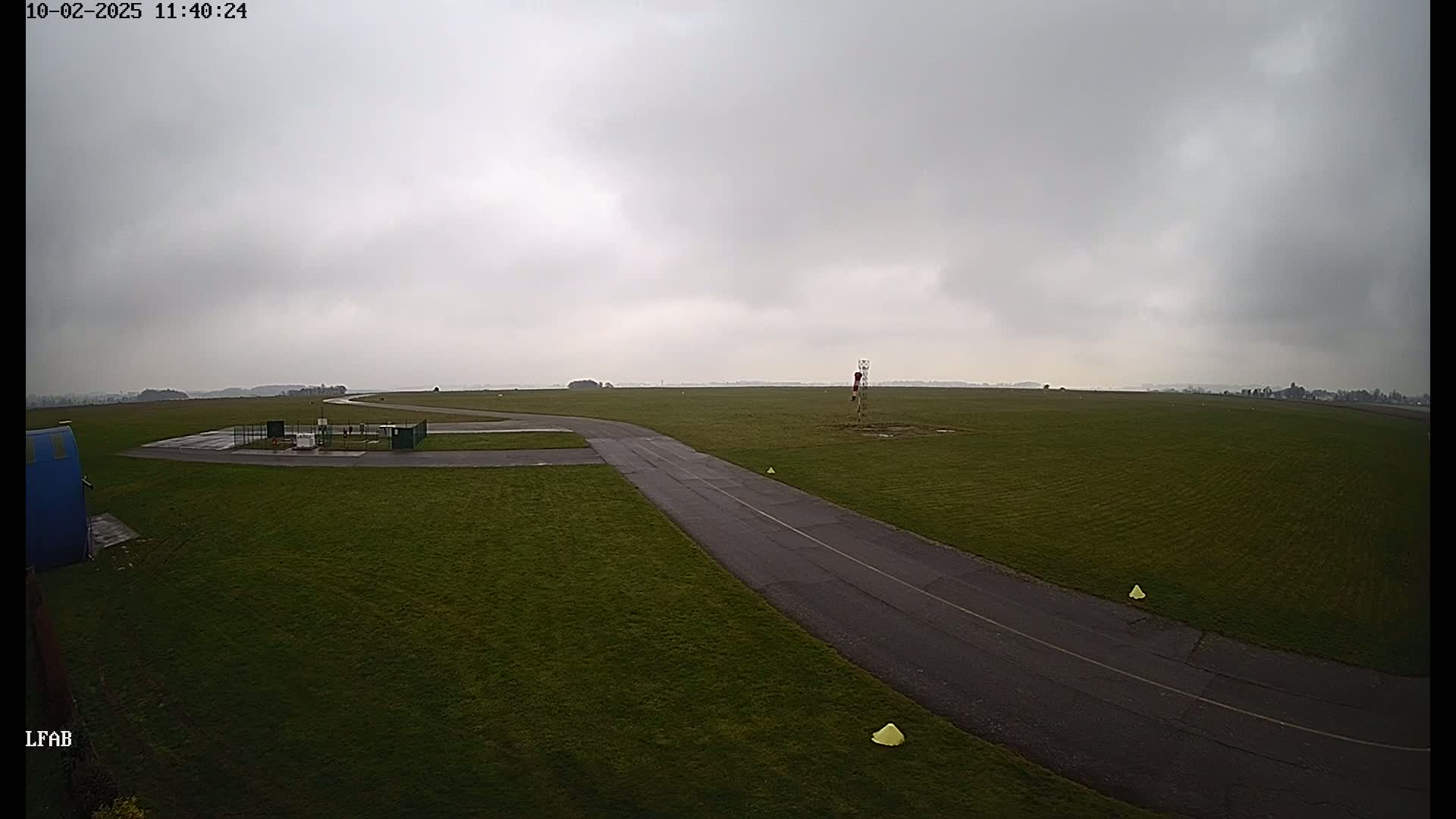 A paved taxiway curves through a grassy airfield under an overcast sky.