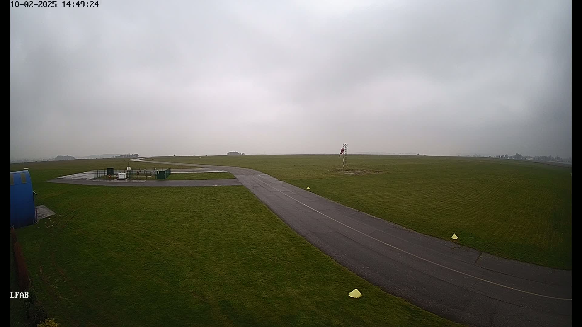 An overcast day reveals a grassy airfield with a paved taxiway curving through the green expanse.
