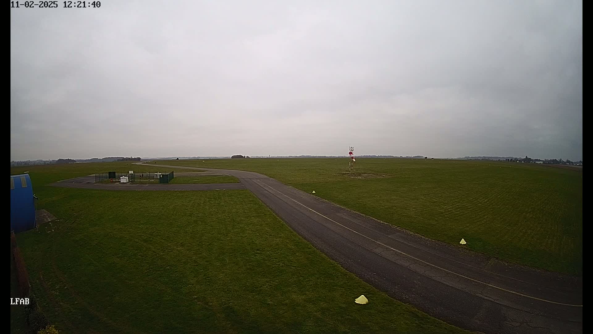 A paved road curves through a grassy airfield under an overcast sky.