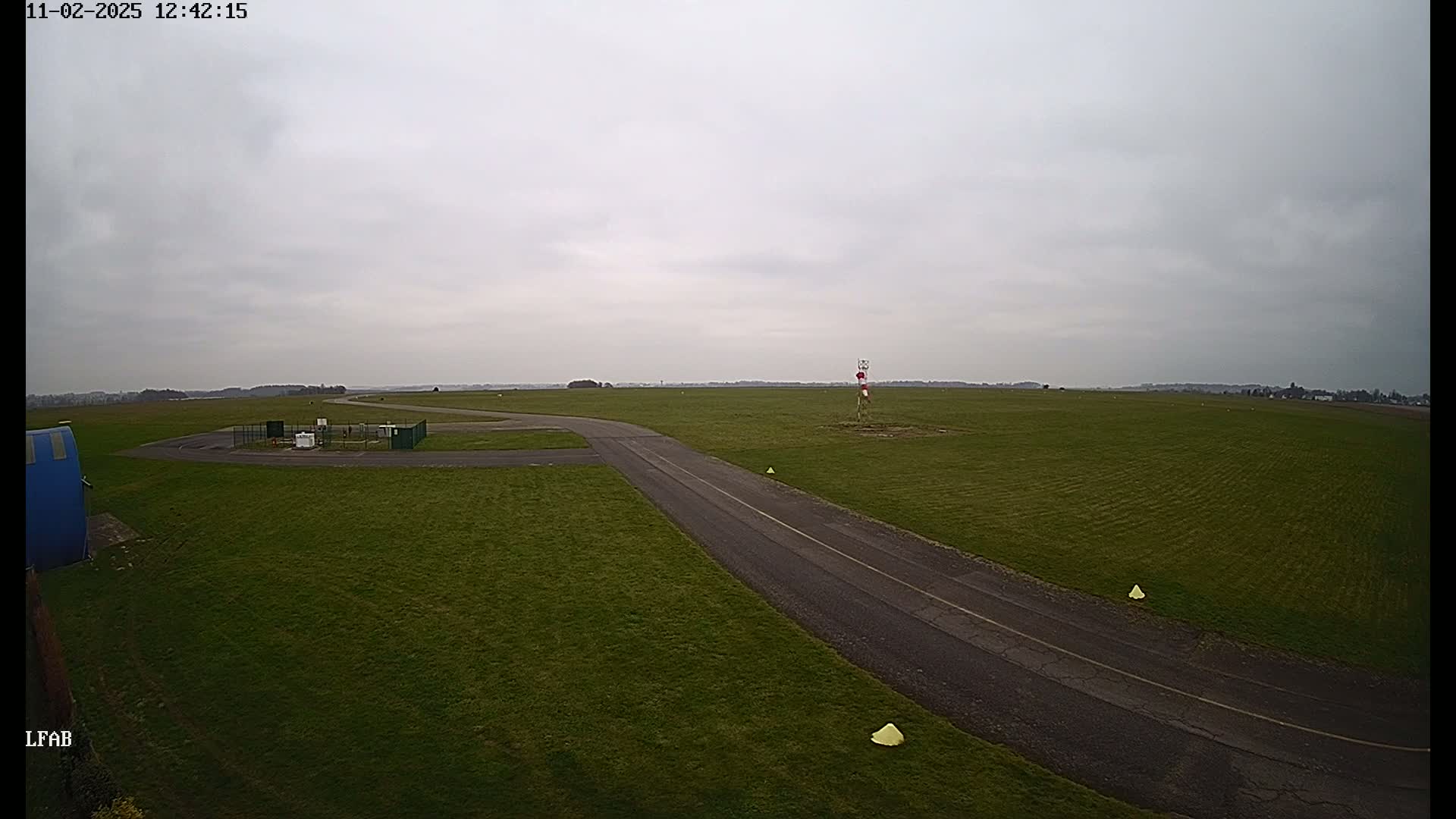 A paved taxiway curves through a grassy airfield under an overcast sky.