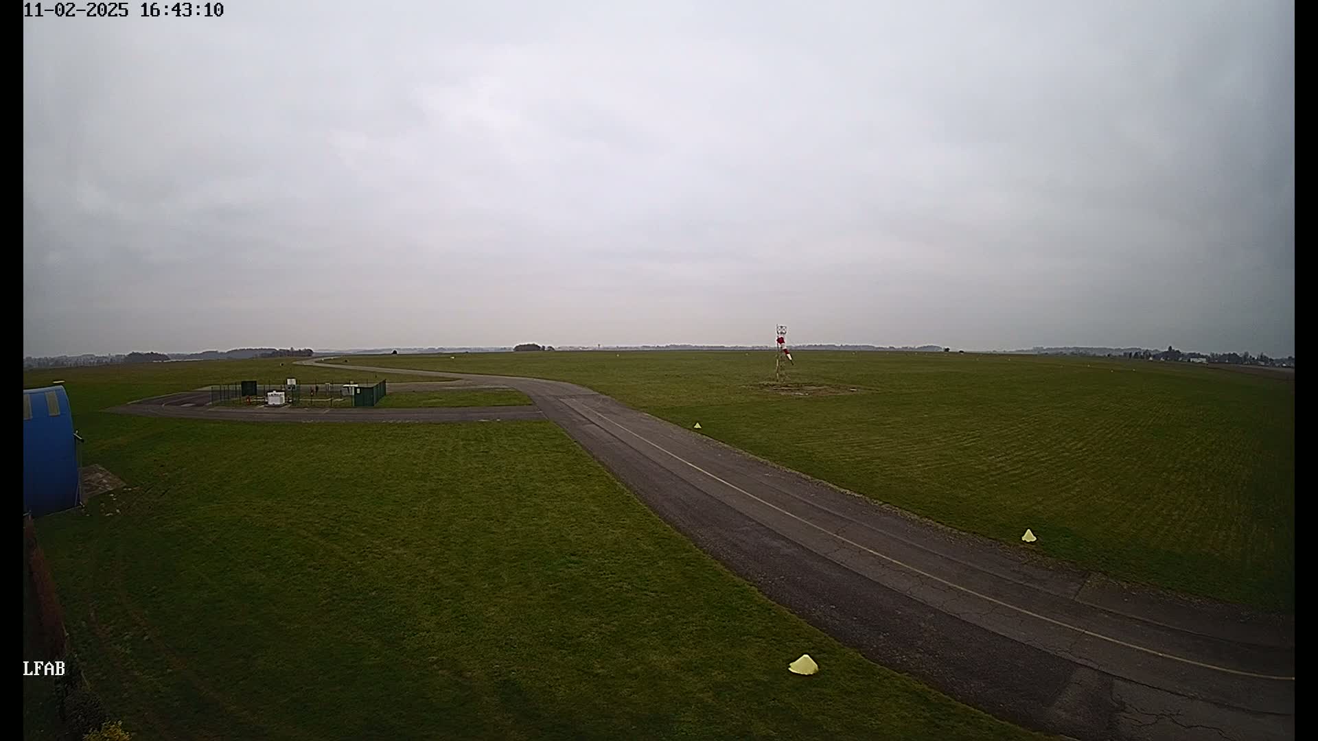 A paved road curves through a grassy airfield under an overcast sky.