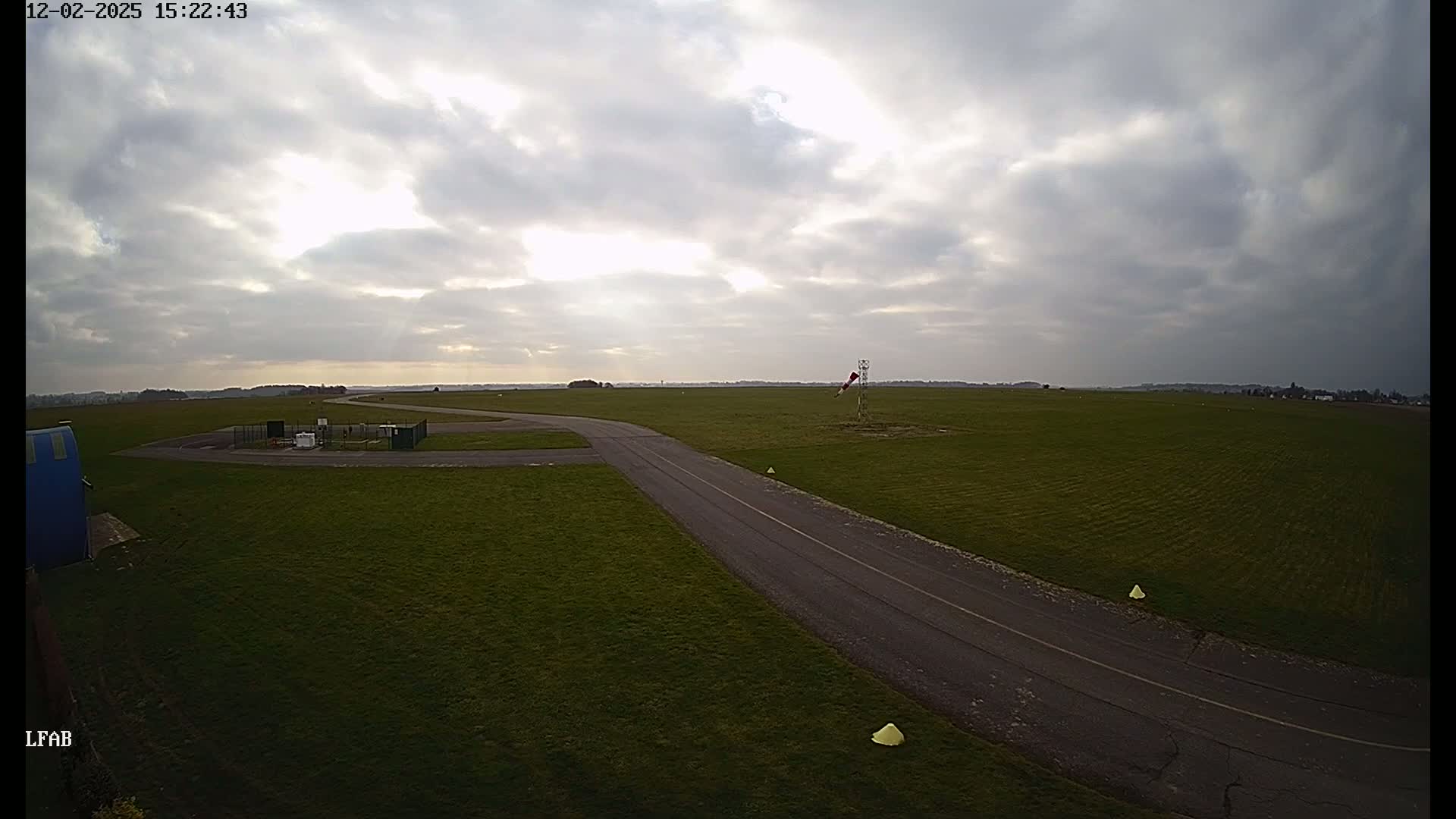 A paved taxiway curves through a grassy airfield under a partly cloudy sky.